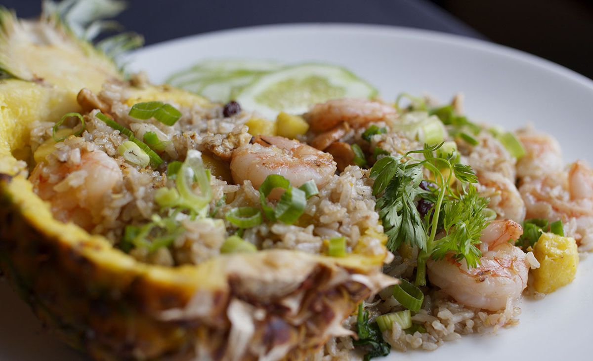 A hollowed out pineapple overflows with shrimp, rice, and herbs on a large plate.