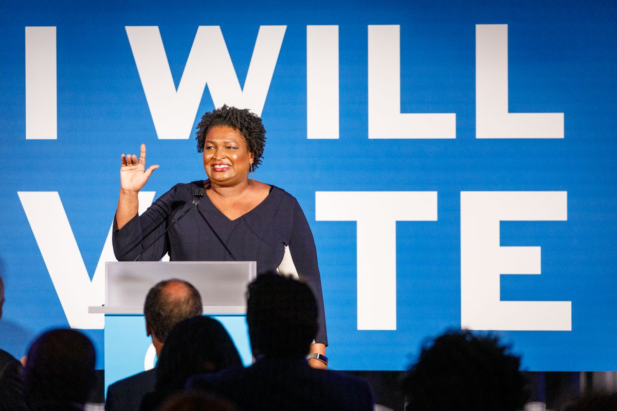 Stacey Abrams onstage in front of a backdrop that reads, “I will vote.”