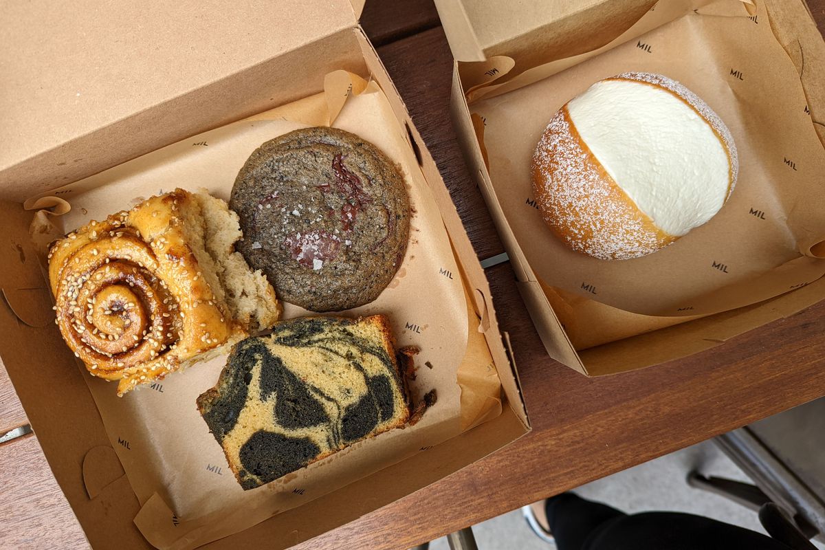 Two cardboard boxes filled with a cinnamon bun, pound cake, cookie, and milk cream bun.