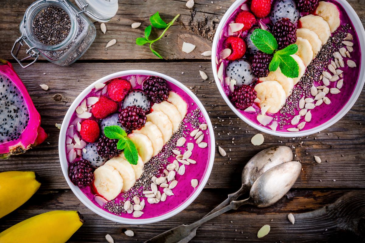 Two blueberry smoothie bowls with banana, raspberry, pitaya, blackberry, almonds, sunflower and chia seeds.