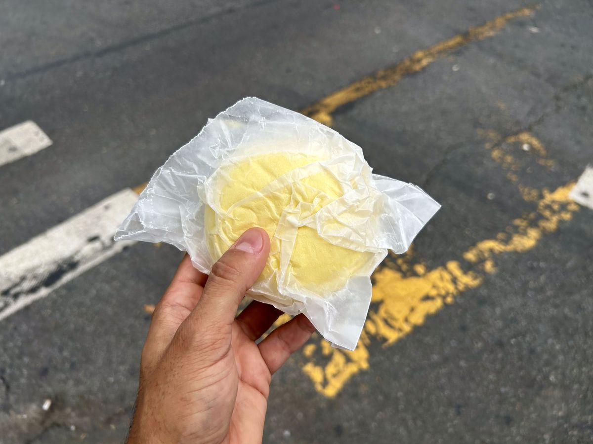 A hand holds a yellow bun against a city crosswalk.