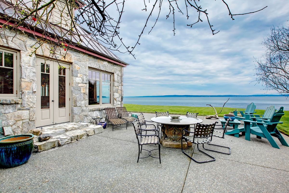 The patio of a stone house on a body of water.