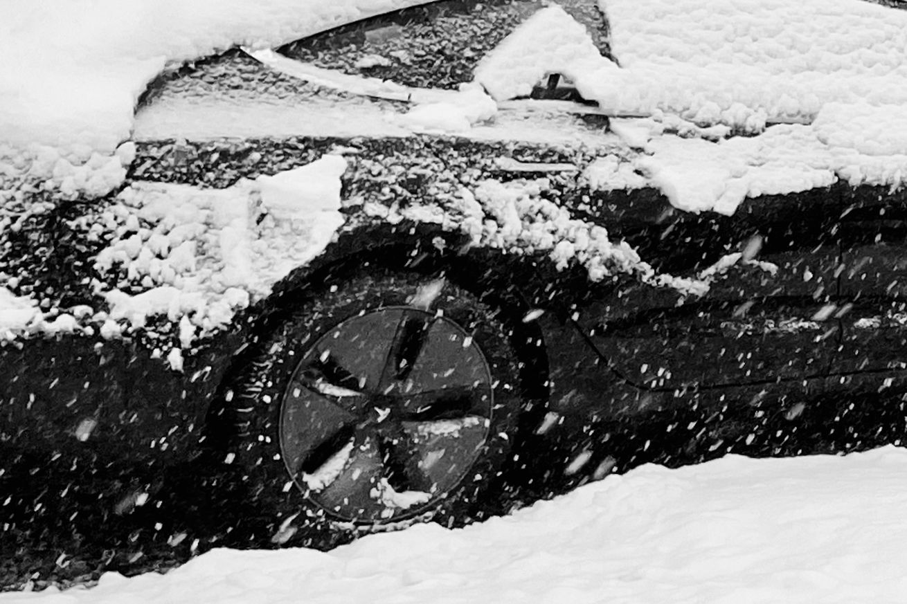 A snowy blizzard is coming down and a Tesla rear wheel and rear door can be seen through a layer of snow sliding off