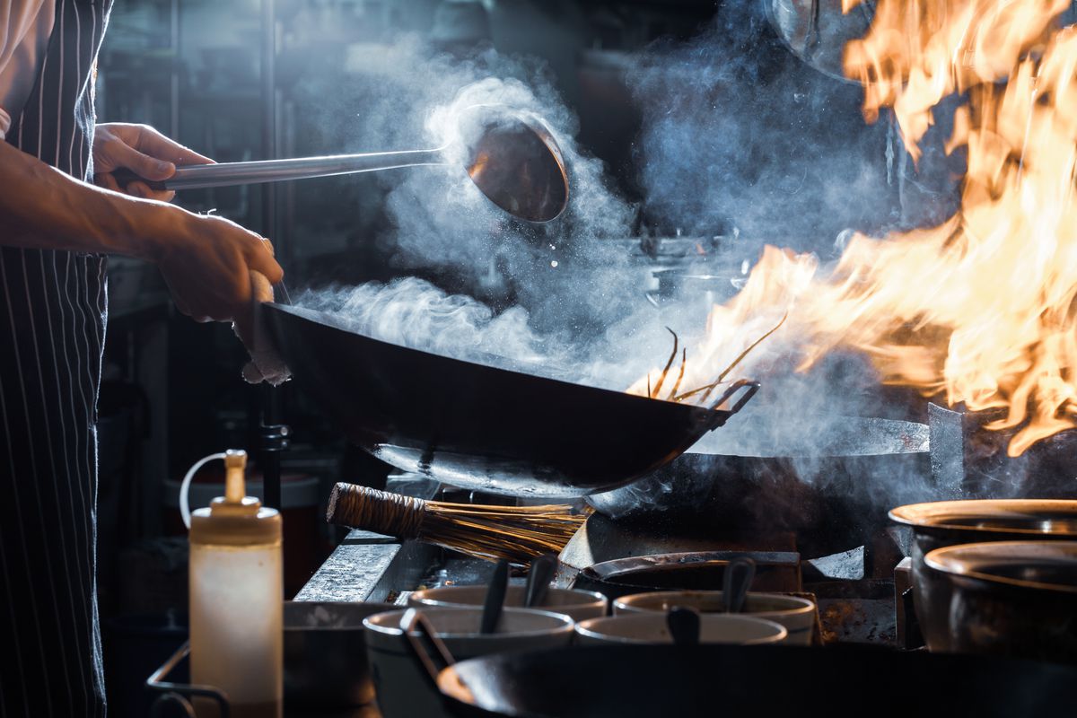 Stock photograph of a chef (bottom half visible) cooking with a fiery wok in a restaurant kitchen