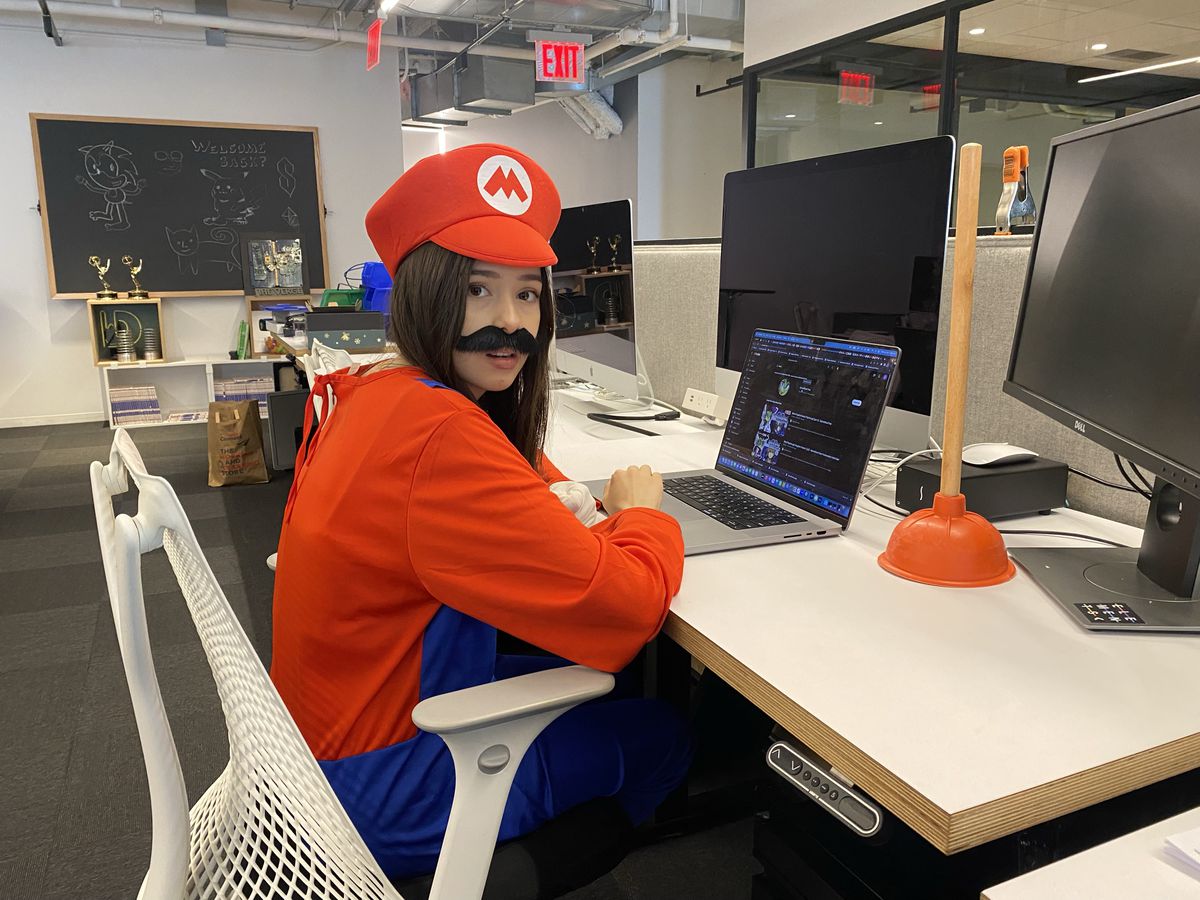 The author sits at an office desk wearing a Mario costume, including his hat and mustache. There is a plunger on the desk to the right of the author’s work laptop.