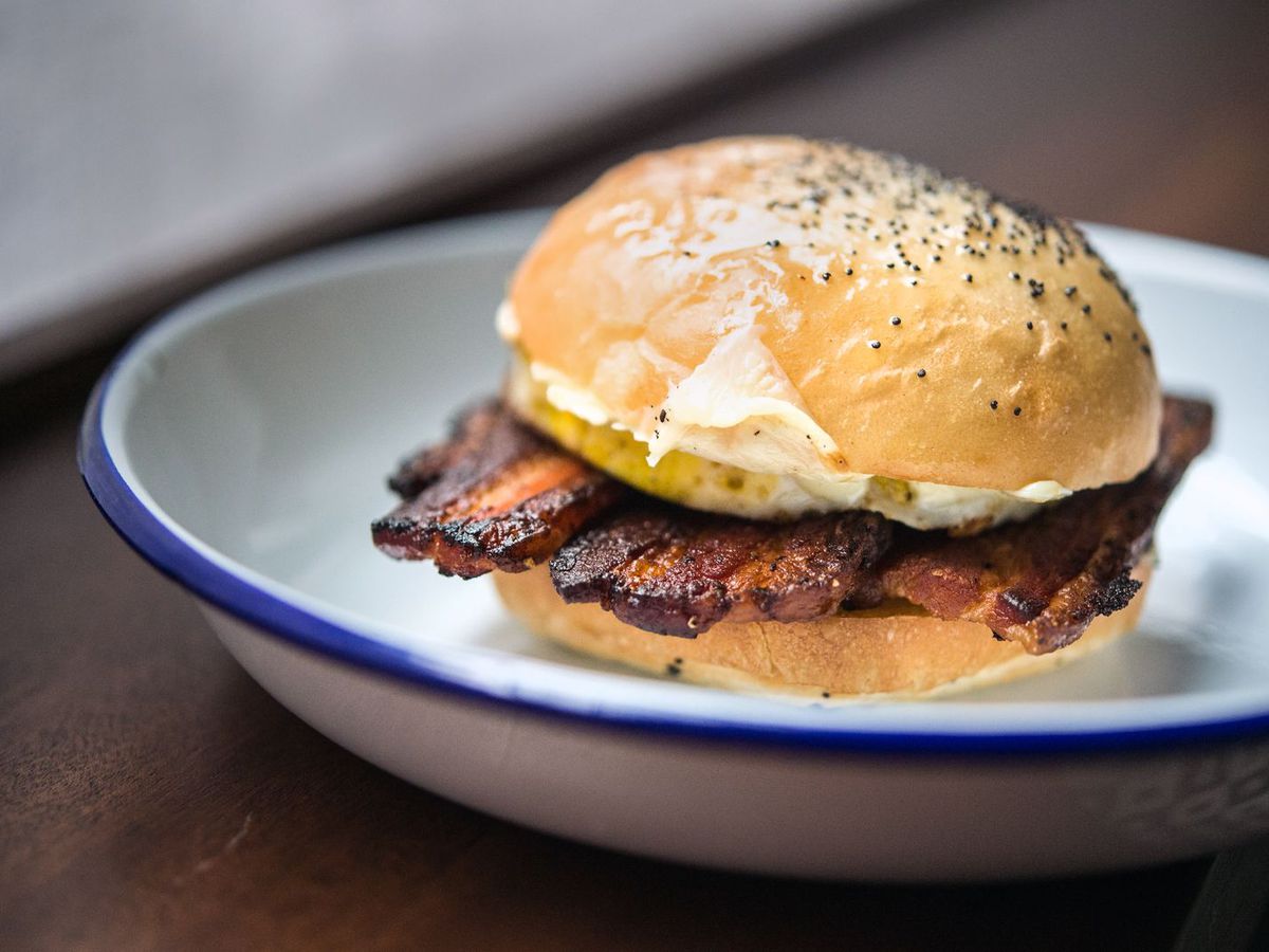 A breakfast sandwich with thick-cut bacon and a poppy seed roll on a blue-rimmed white plate