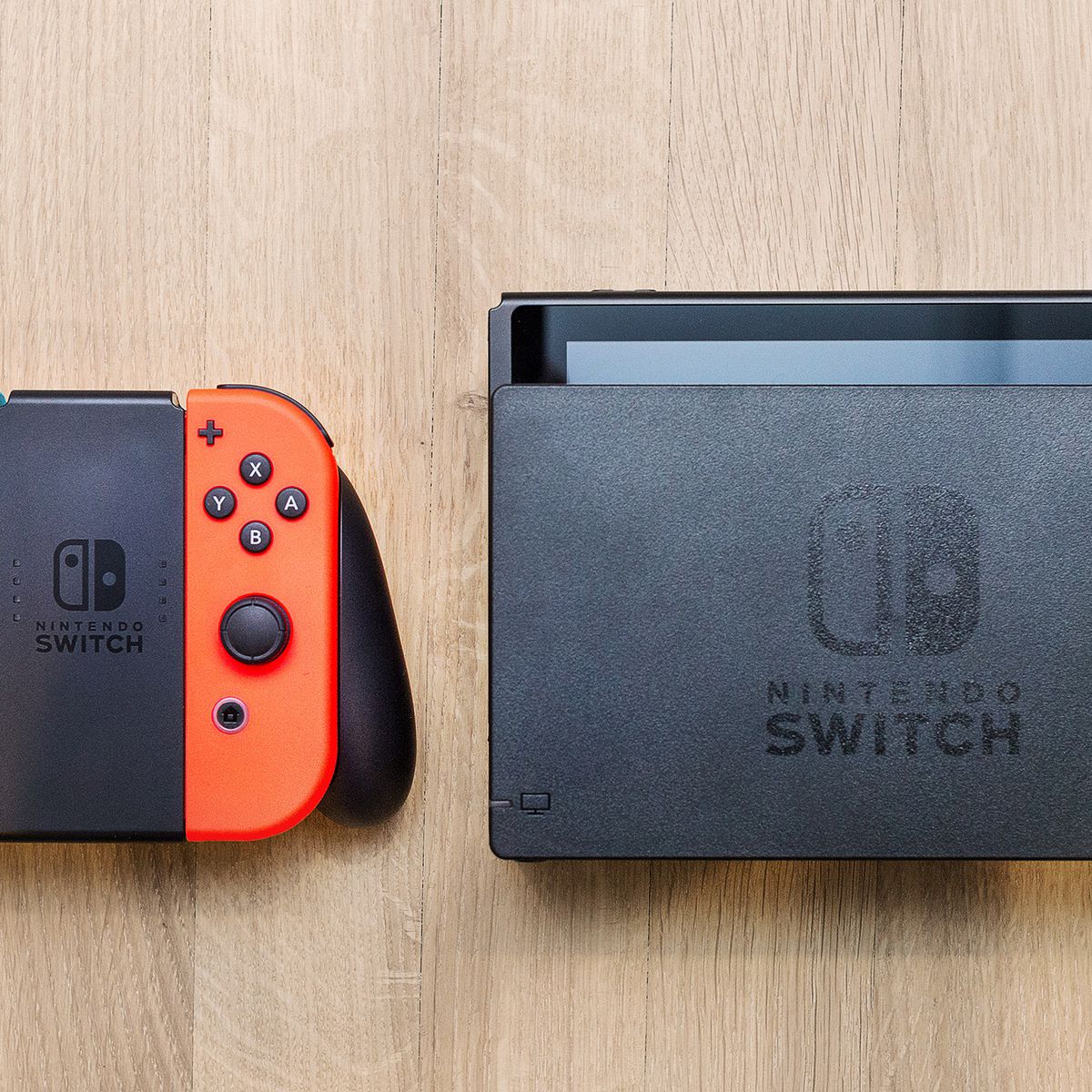 Nintendo Switch - Neon Red/Blue Joy-Cons in Joy-Con Grip next to Dock, all sitting on a wooden background