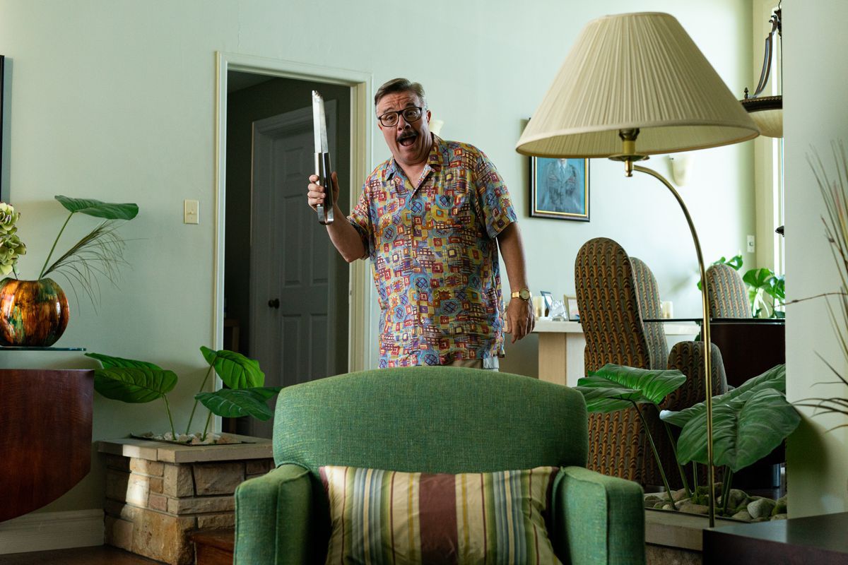 Nathan Lane, in a Hawaiian-style shirt, holds something that looks sort of like a weapon, though it’s actually a grill utensil.