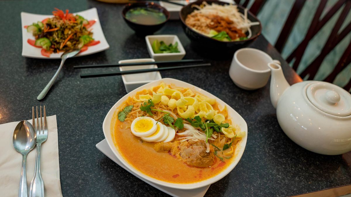 A dark table with a bowl of noodle soup, rice noodle stir fry, tea leaf salad, and miso soup.