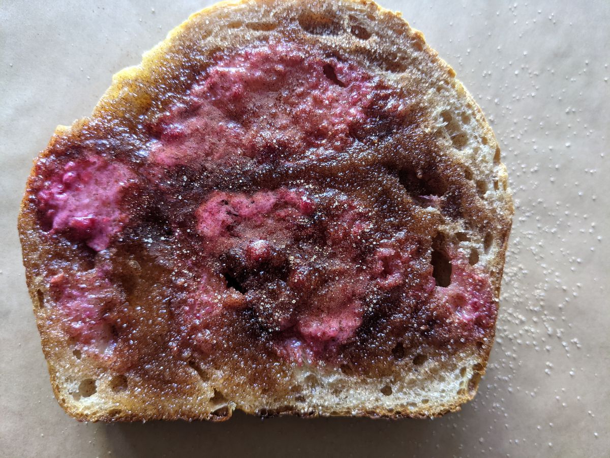 A thick piece of toast is spread with a pinkish fruit butter and cinnamon sugar. It’s sitting on a light background.