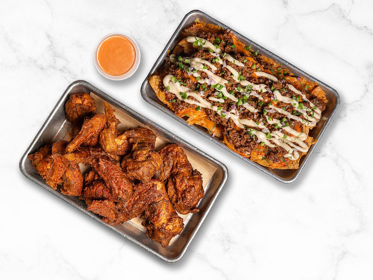 A tray of chicken wings next to a tray of nachos