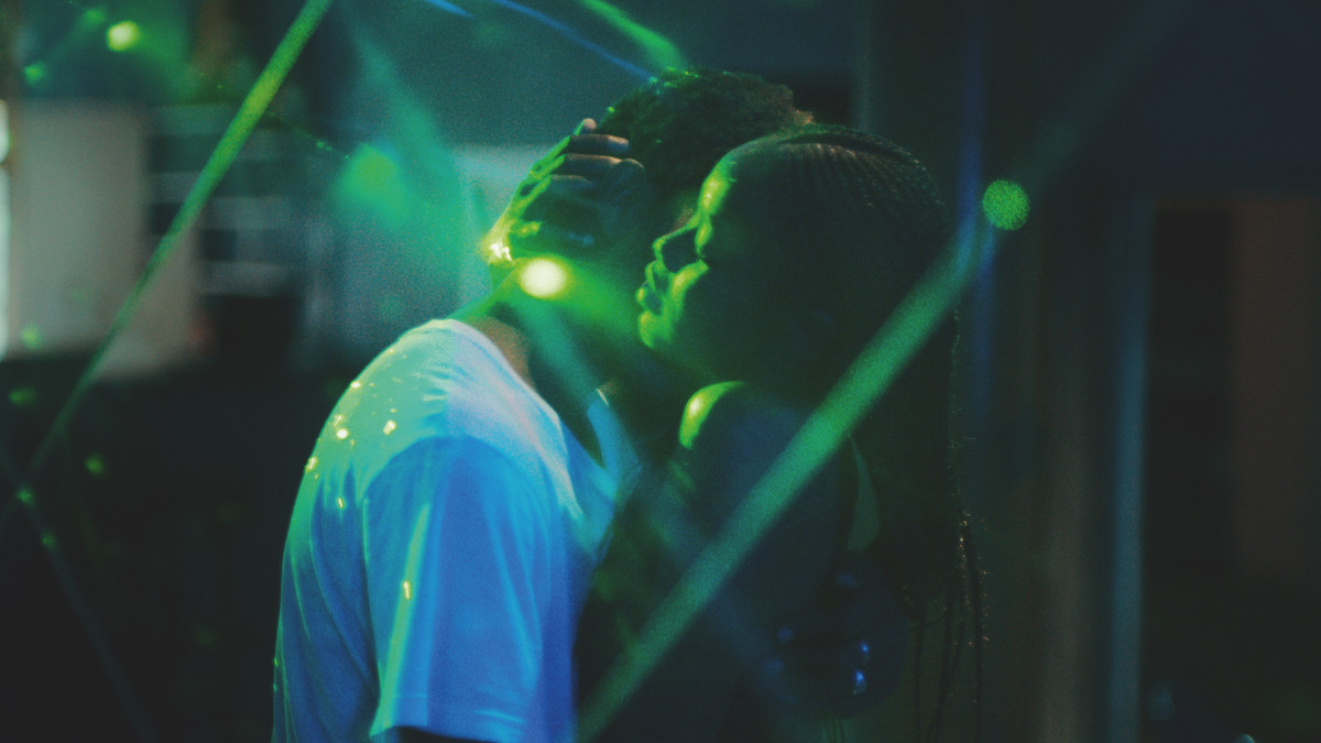 Two figures hold each other close on a dance floor, as neon green lights bounce off of them, in Atlantics