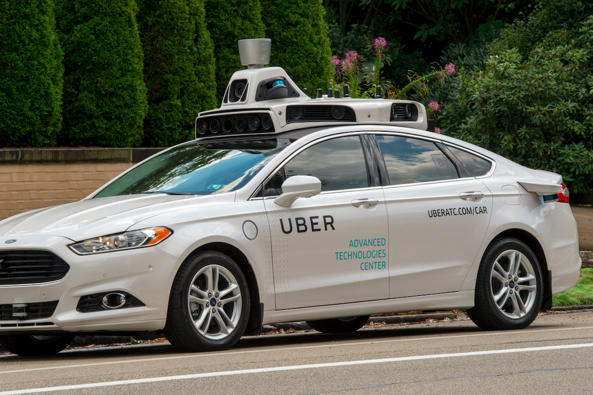 An Uber self-driving model car is shown parked by a tree-lined sidewalk. 