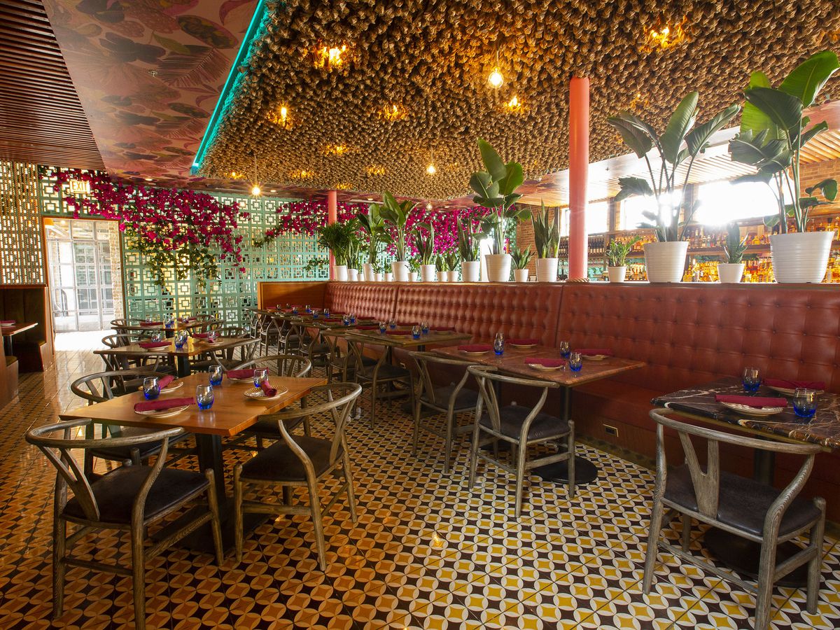 A restaurant dining room filled with plants and tables and chairs on a tile floor.