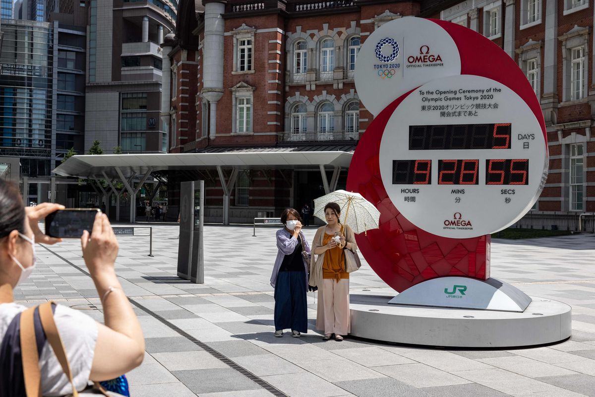 People take a picture of the countdown clock for the Tokyo 2020 Olympic Games displaying 5 days and 9 hours to go to the opening ceremony, outside Tokyo station in Tokyo on July 18, 2021.