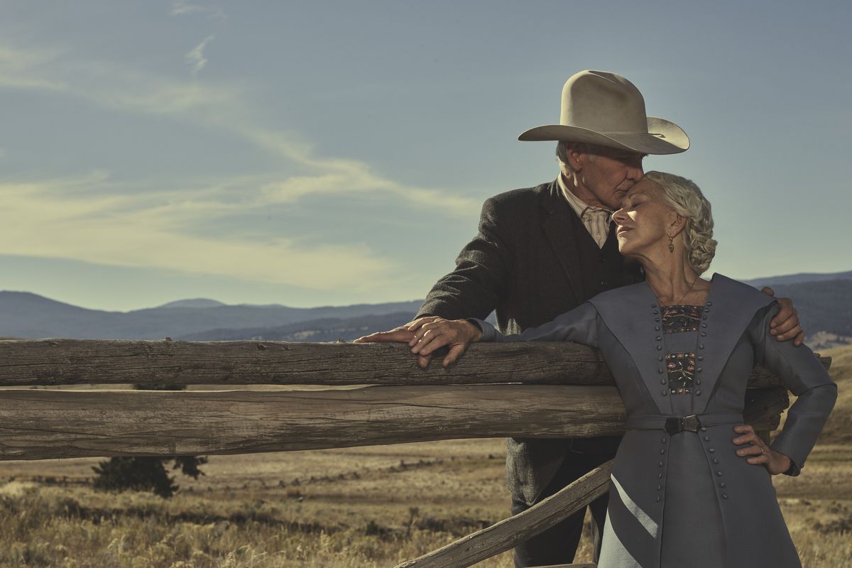 Helen Mirren leans against a fence post on the prairie as Harrison Ford stands behind her and kisses her head in the key art for the Yellowstone prequel 1923.