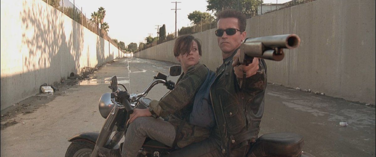 (LR) ادوارد فورلونگ و آرنولد شوارتزنگر در نقش جان کانر و یک ترمیناتور T-800 بازبرنامه‌ریزی شده که یک تفنگ ساچمه‌ای را در بالای موتورسیکلتی در دست دارد که در دره‌ای در حال بیکاری در ترمیناتور 2: روز داوری است. 