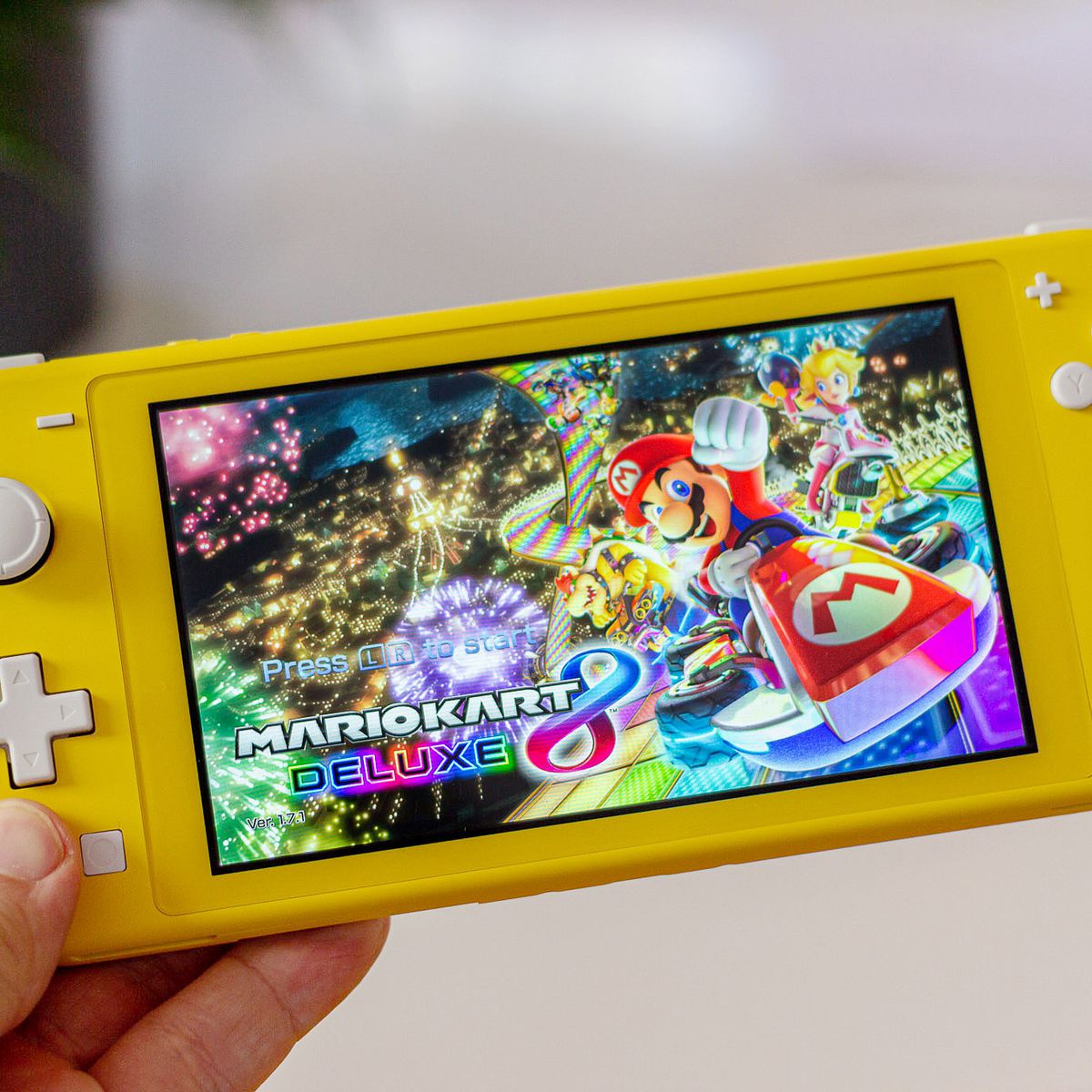 a hand holding a yellow Nintendo Switch Lite showing Mario Kart 8’s title screen
