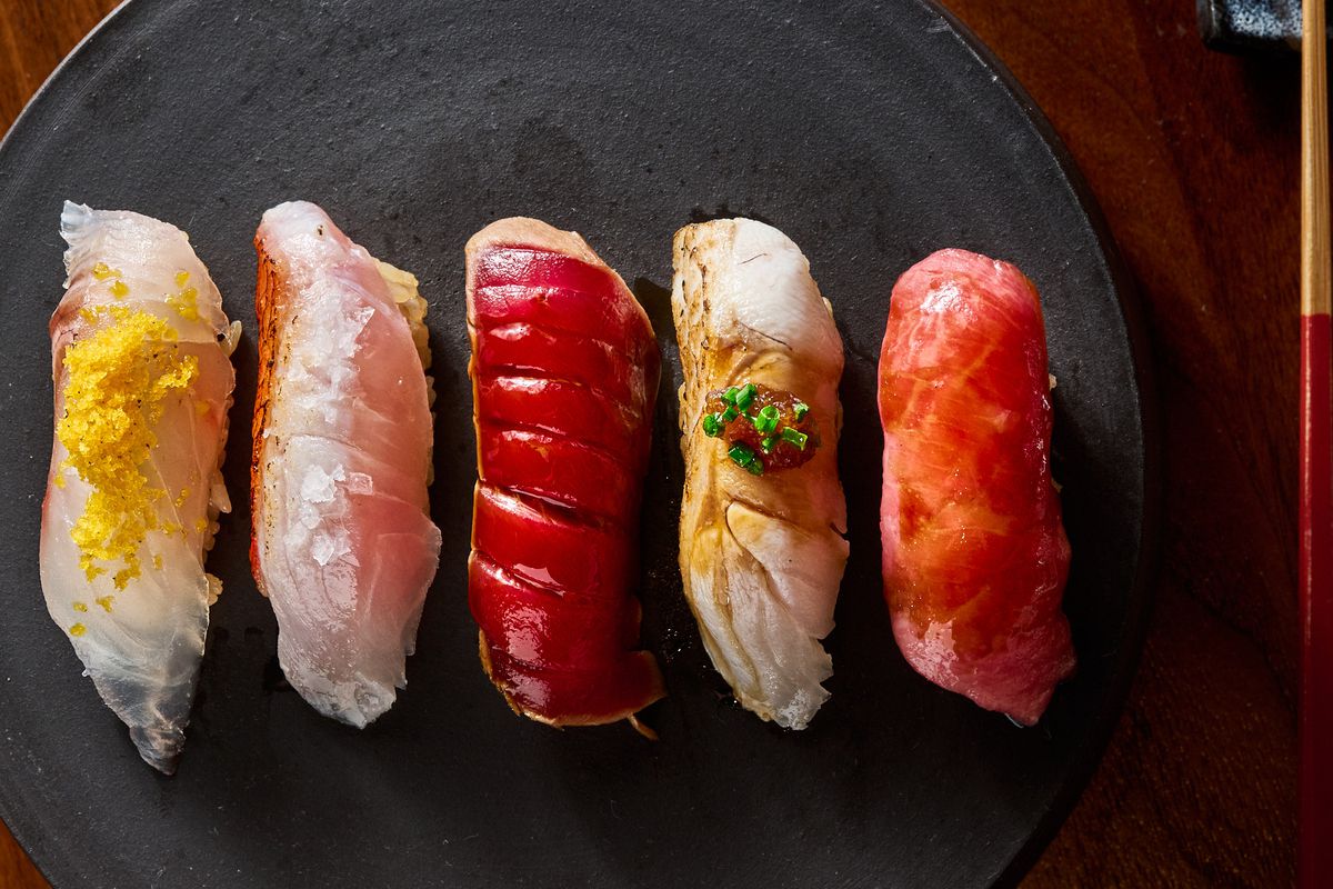 Five different kinds of nigiri sushi on a black plate.