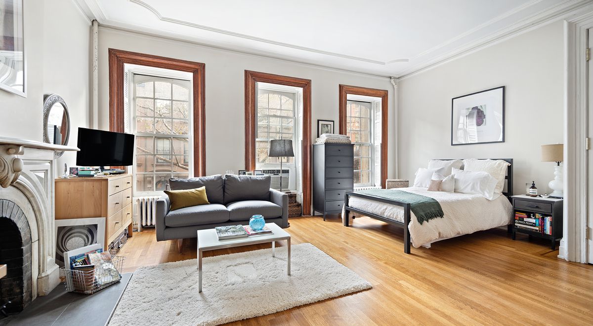 A bedroom with hardwood floors, three large windows, a fireplace, and decorative moldings.