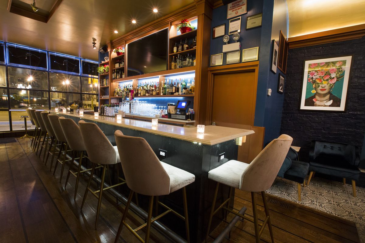 A long white bar with white stools in a blue bar space.