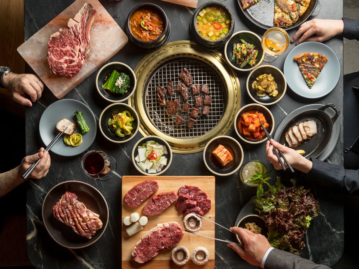 An overhead photograph of plates of banchan surrounding a Korean barbecue grill