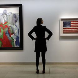An auction house worker poses for photographers between a 1961 Pablo Picasso painting, left, and an encaustic Stars and Stripes painting entitled \'Flag\', right, made between 1960-1966 by U.S. artist Jasper Johns, in central London, Feb. 5, 2010.