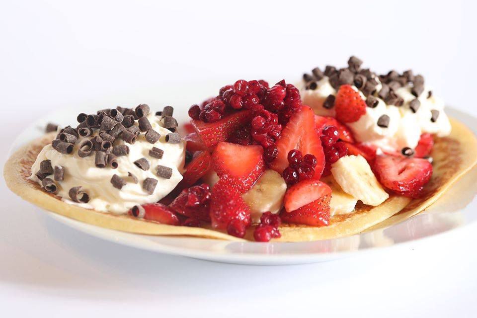 Thin pancakes are topped with huge piles of whipped cream, strawberries, and some chocolate chips