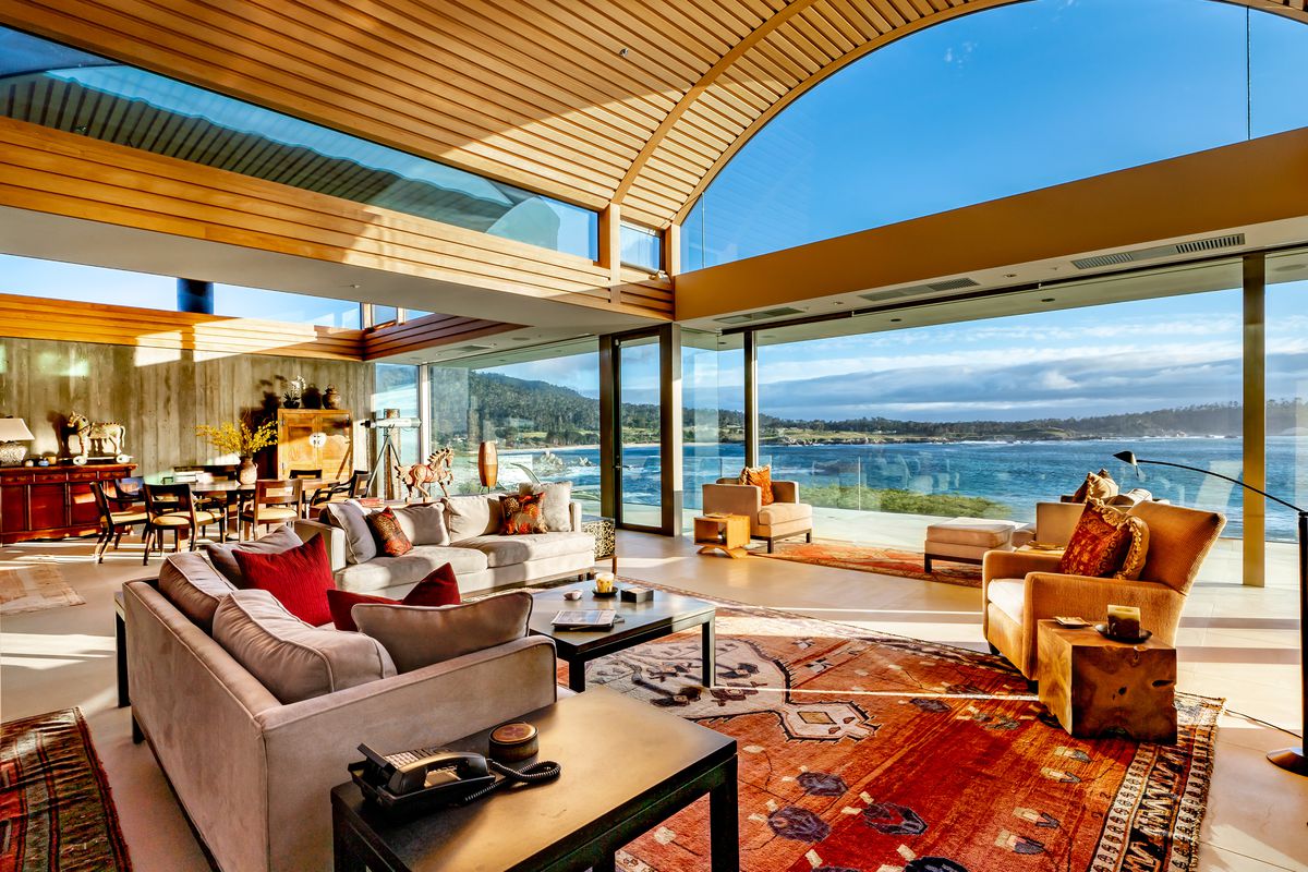 An interior view of a living room in a Carmel house for sale with a barrel vaulted wood ceiling and ocean views. There is a couch and other chairs.