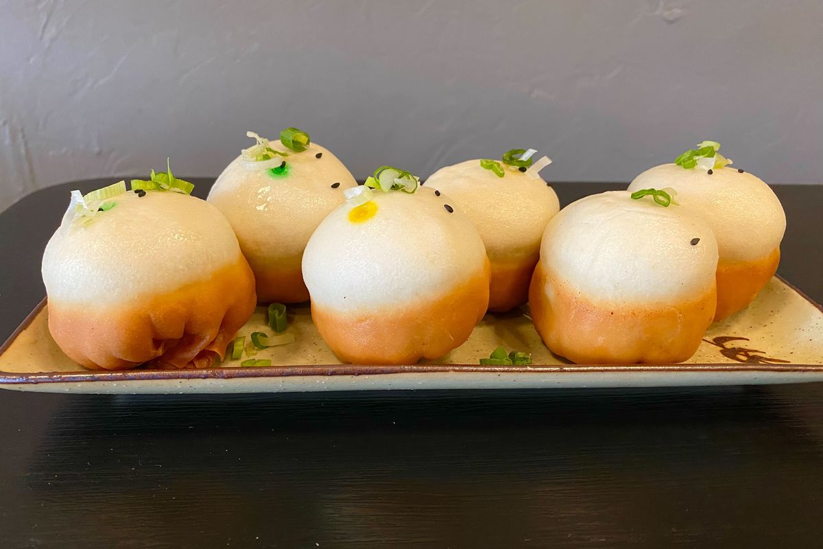 Six white buns with golden crusts on the bottom on a plate.