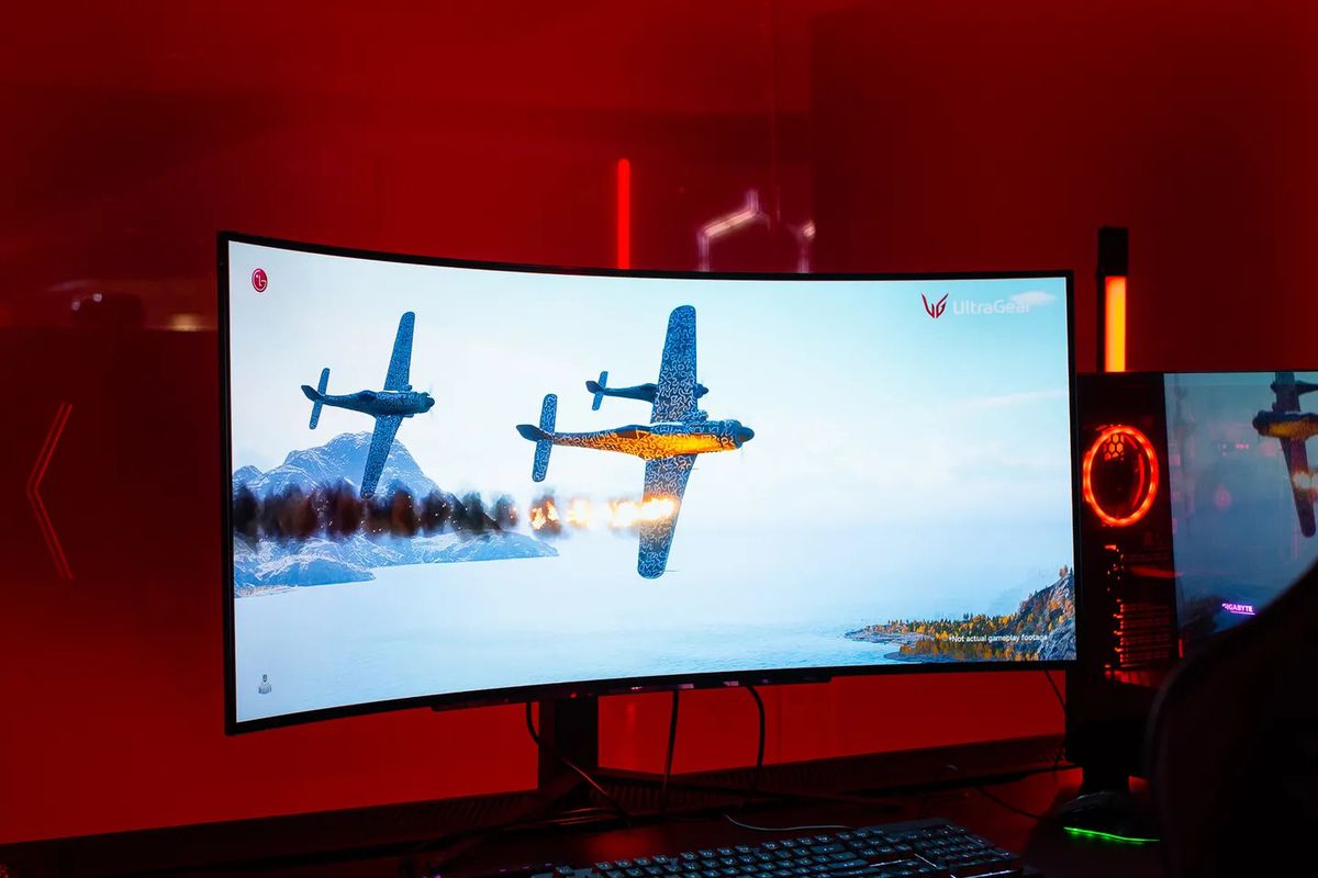 An image featuring the 45-inch LG UltraGear OLED gaming monitor. The setting is a dark red room, and there’s an airplane dogfighting scene displaying on the monitor.