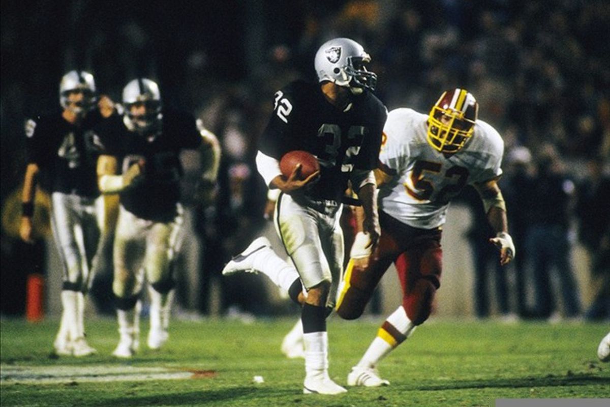 Los Angeles Raiders running back Marcus Allen (32) is pursued by Washington Redskins linebacker Neal Olkewicz (52) during Super Bowl XVIII at Tampa Stadium.