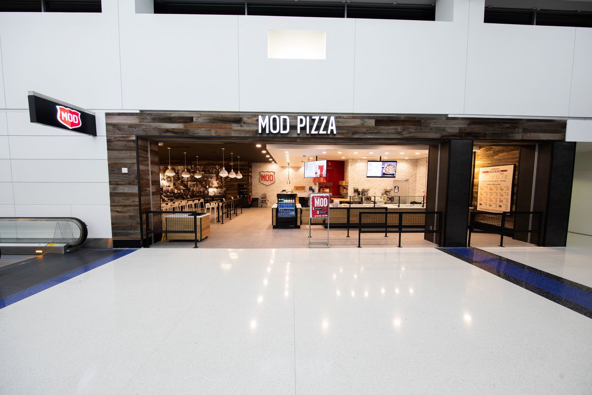 A photo of the wood-paneled storefront for Mod Pizza in the white-walled North Terminal.