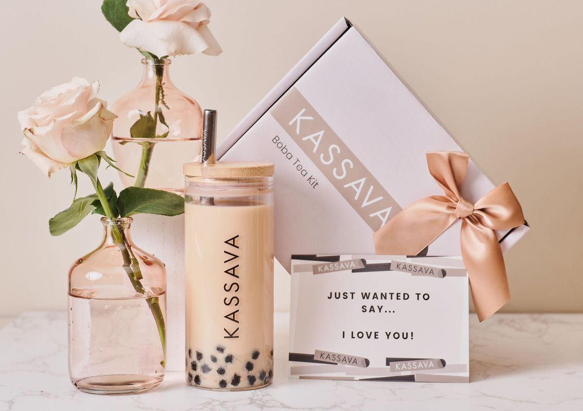 A pair of boxes sit next to a glass with boba tea and a vase with a rose in it.