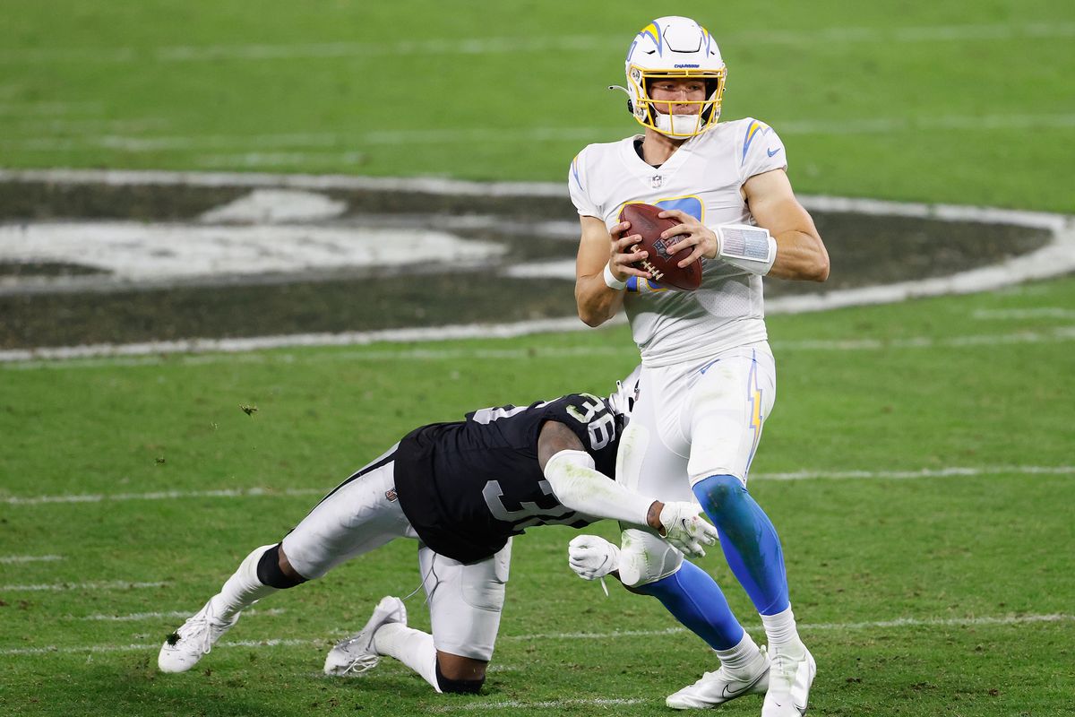 Quarterback Justin Herbert #10 of the Los Angeles Chargers avoids a tackle from cornerback Daryl Worley #36 of the Las Vegas Raiders during the NFL game at Allegiant Stadium on December 17, 2020 in Las Vegas, Nevada.