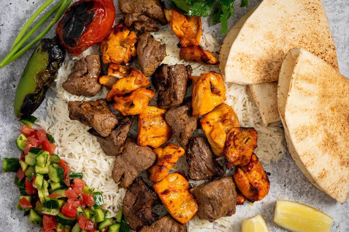 A close up shot of grilled skewers of meat over rice with pita.