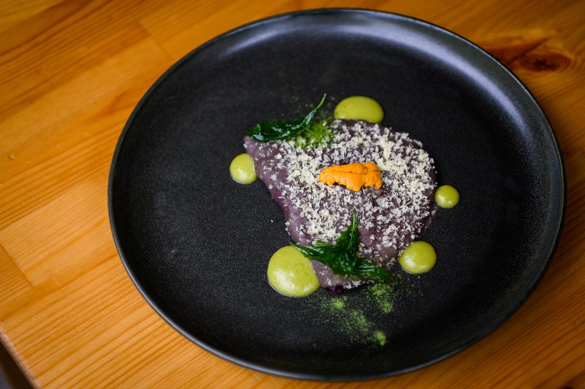 A black plate comes topped with a purple bean-covered tortilla, with dots of avocado salsa and a small tongue of uni. 