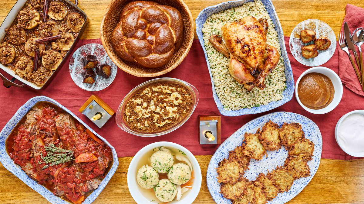 A robust holiday spread for Rosh Hashanah featuring dishes over a red cloth, including braided challah, apple honey-glazed chicken, baked apples, and roasted squash and carrots.