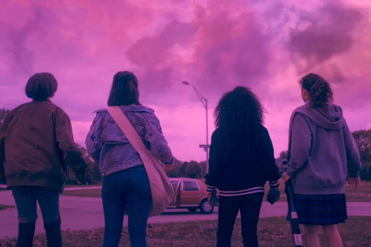 Paper Girls - Four newspaper delivery girls look up at ominous purple skies in a suburban neighborhood