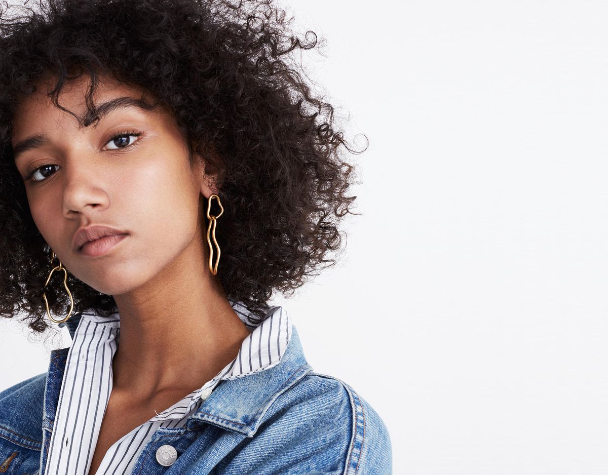 A model in a denim jacket and gold earrings