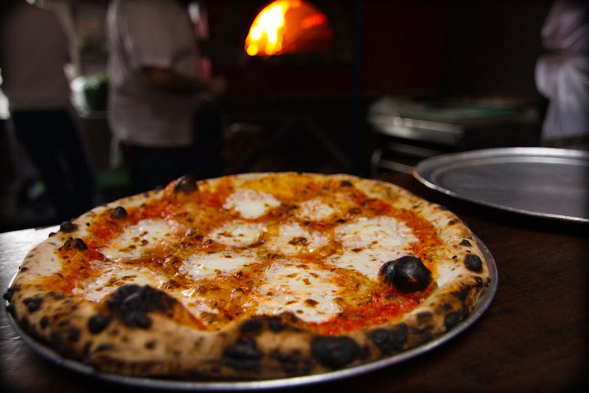 A wood-fired pizza being placed in the oven.