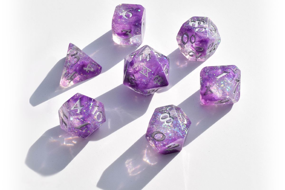 Image of a seven dice set: a D4, D6, D8, D10, D12, D20, and D100. The dice have a galaxy swirl inside them of dark purple, light purple, and clear with iridescent glitter flakes. The numbers are painted silver. The D20 has the BoB sigil on the 20 side.