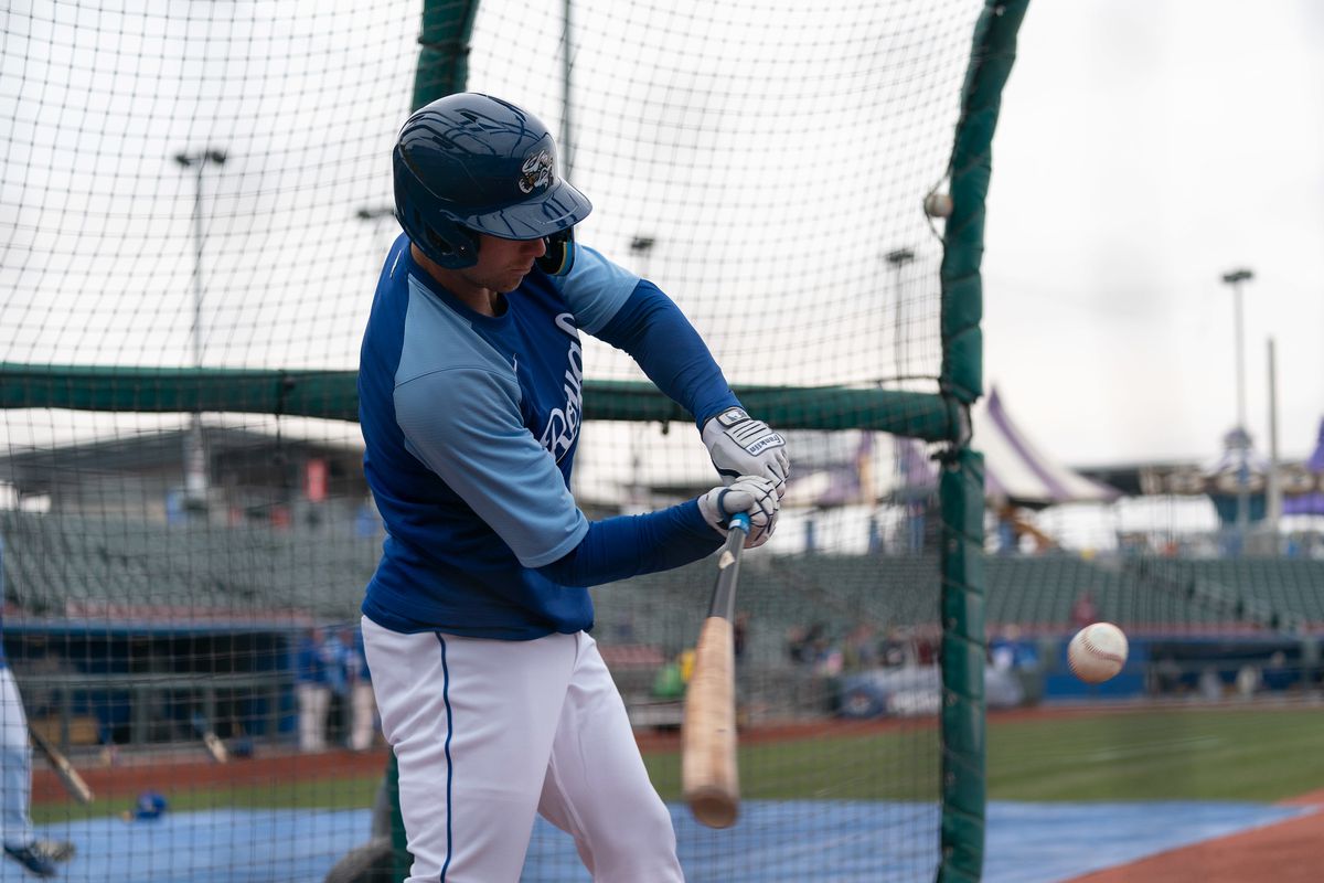 A right-handed batter in a batting practice cage swinging, about to make contact with the ball, which is also in the frame.
