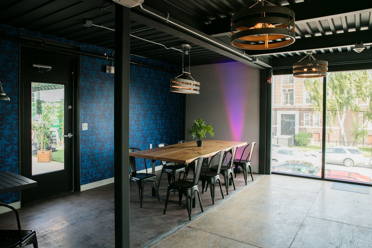 A long communal table with metal chairs sits next to a wall with blue wallpaper in an industrial space.