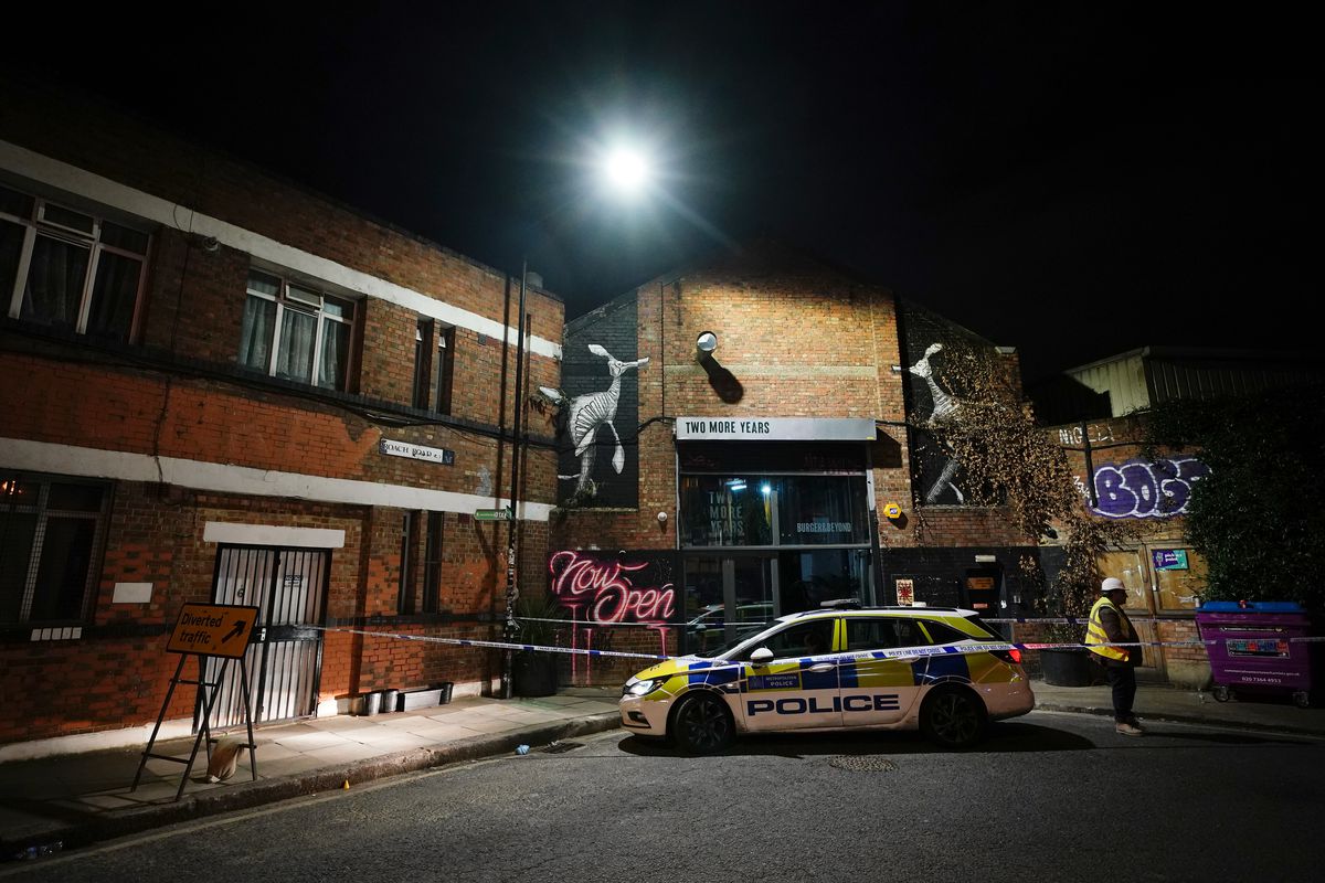 At night under street lights, a police car sits outside Two More Years bar in Hackney Wick