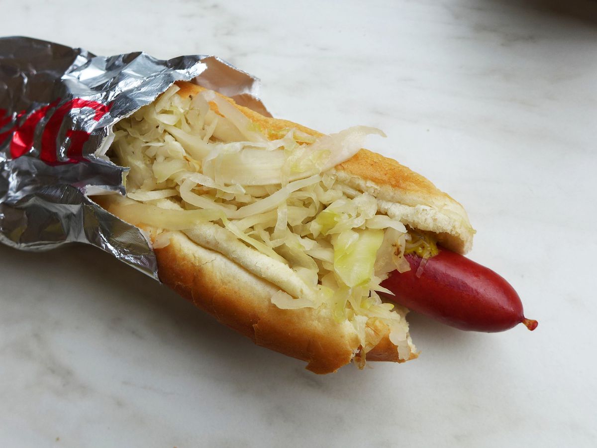 A hot dog with heaped kraut sticking out of a metallic sleeve.