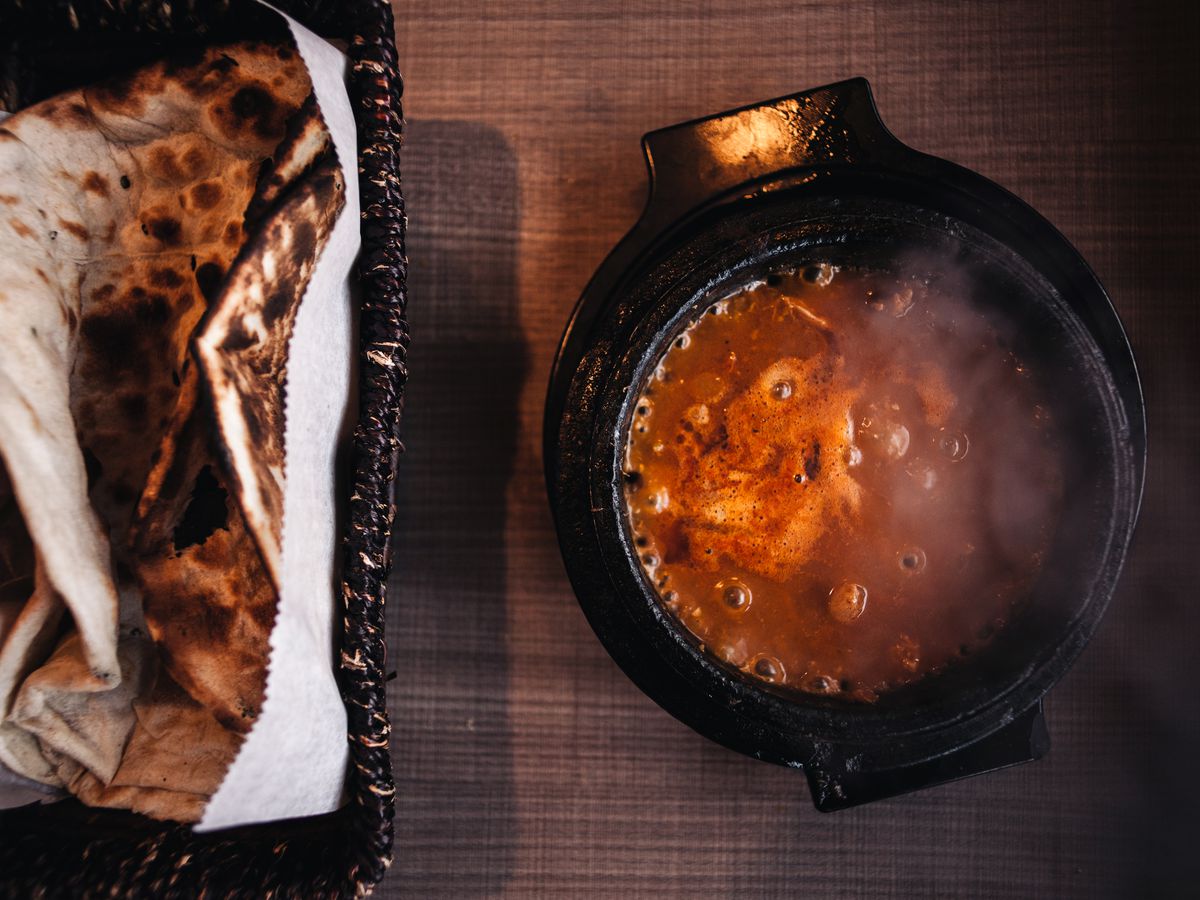 A boiling bowl of a red stew with flatbreads.