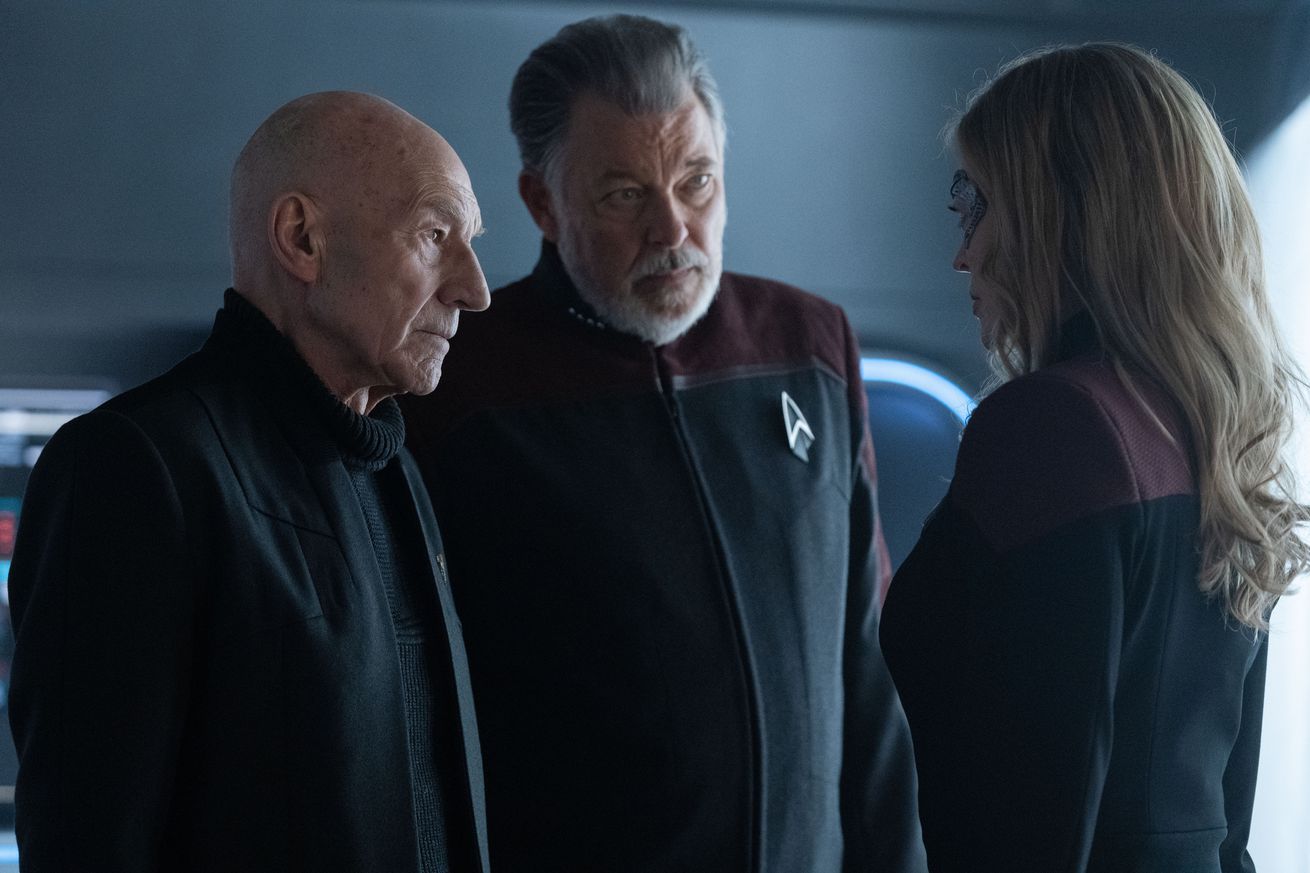 Two old men stare at a younger blond woman. They are all dressed in Star Trek uniforms.