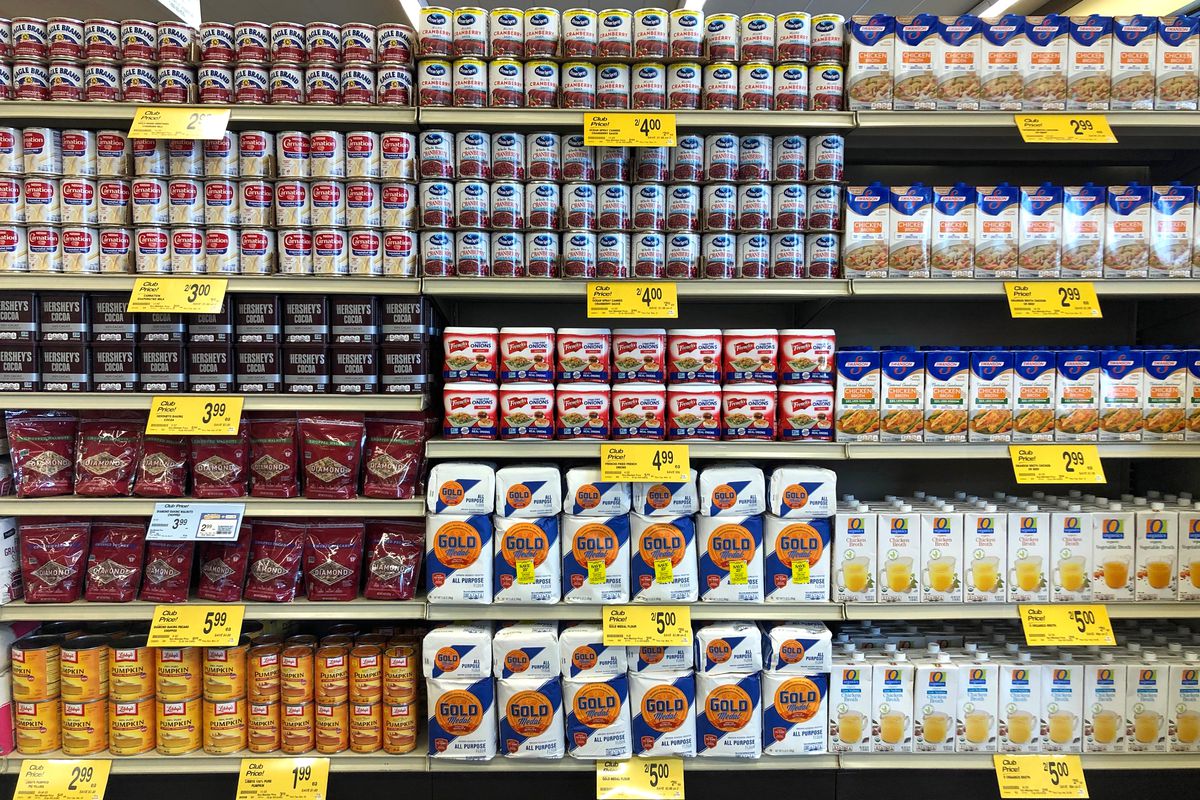 Grocery store shelves with cans of condensed milk, chocolate, pumpkin puree, cranberry sauce, flour 