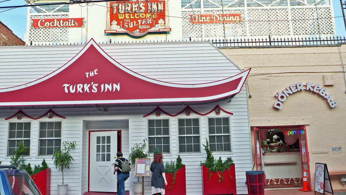 The Turk’s Inn restaurant is inside a building that looks like a white house, with a red awning and a neon “Turk’s Inn” sign up top.